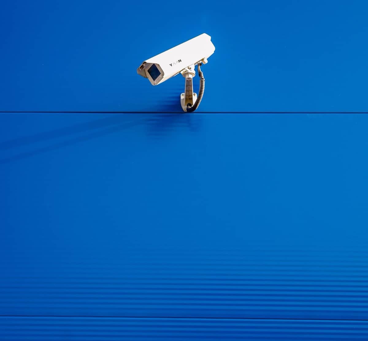 Caméra de vidéosurveillance blanche fixée sur un mur bleu